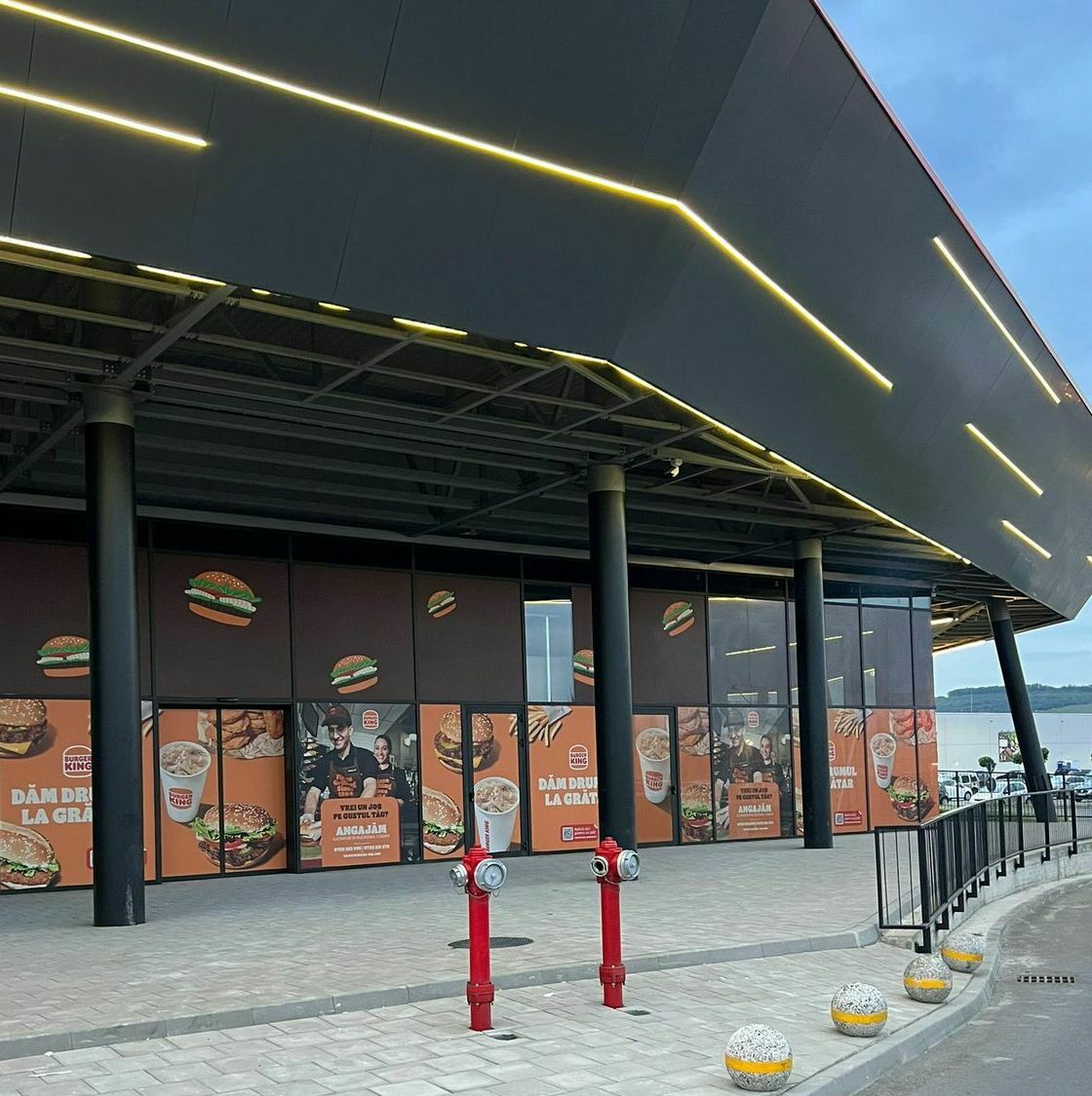 Decorare fațadă mall cu autocolant și mesh pentru Burger King Implementarea unei soluții vizuale de impact pentru fațada unui mall important, prin aplicarea autocolantului și mesh-ului personalizat pentru renumitul lanț Burger King, incluzând procese meticuloase de printare, design grafic și montaj profesionist.